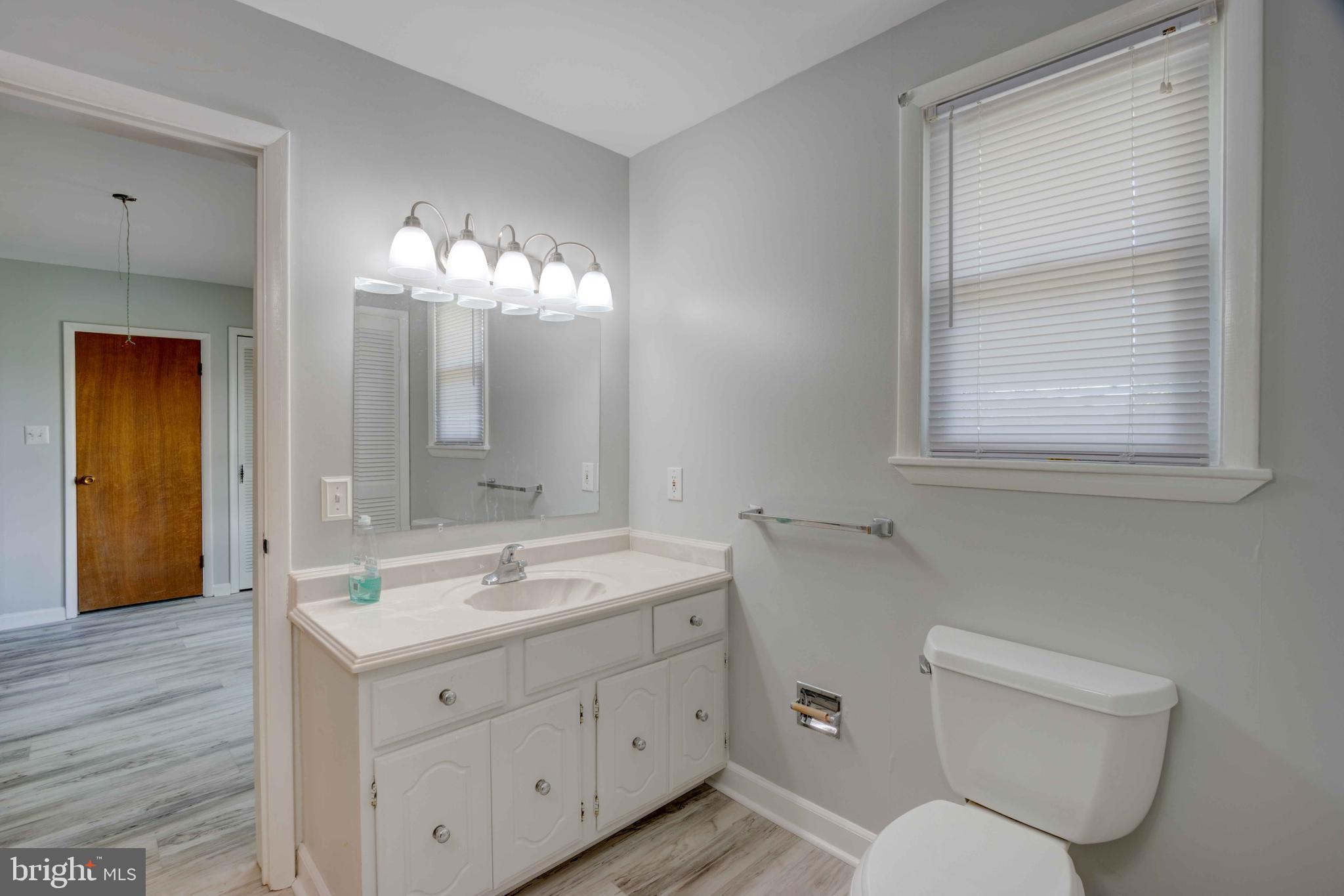 625 Hammonds Lane Baltimore, MD 21225 - Photo 9 of 40 a bathroom with a toilet a sink a mirror a window and vanity