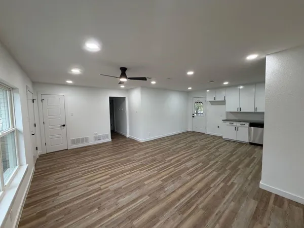 a view of an empty room with wooden floor and a kitchen