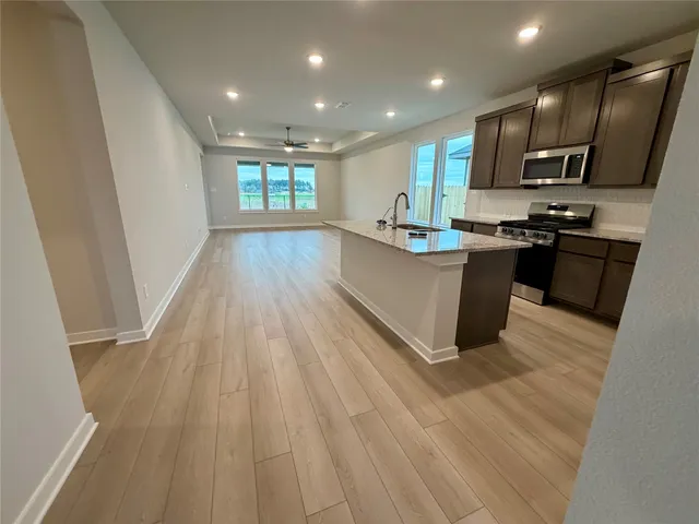 a kitchen with stainless steel appliances granite countertop a refrigerator a sink dishwasher a stove and a oven with wooden floor