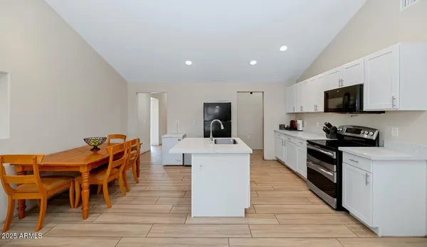 a kitchen with stainless steel appliances kitchen island granite countertop a stove top oven a sink a dining table and chairs with wooden floor