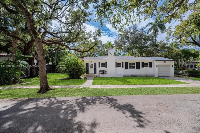 a view of a white house next to a yard with a large trees