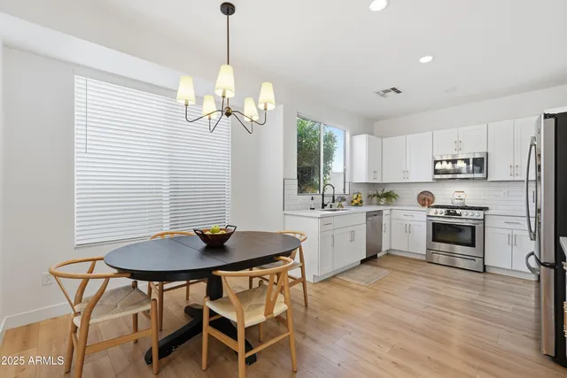 a kitchen with stainless steel appliances a white refrigerator a stove a oven a dining table and chairs with wooden floor