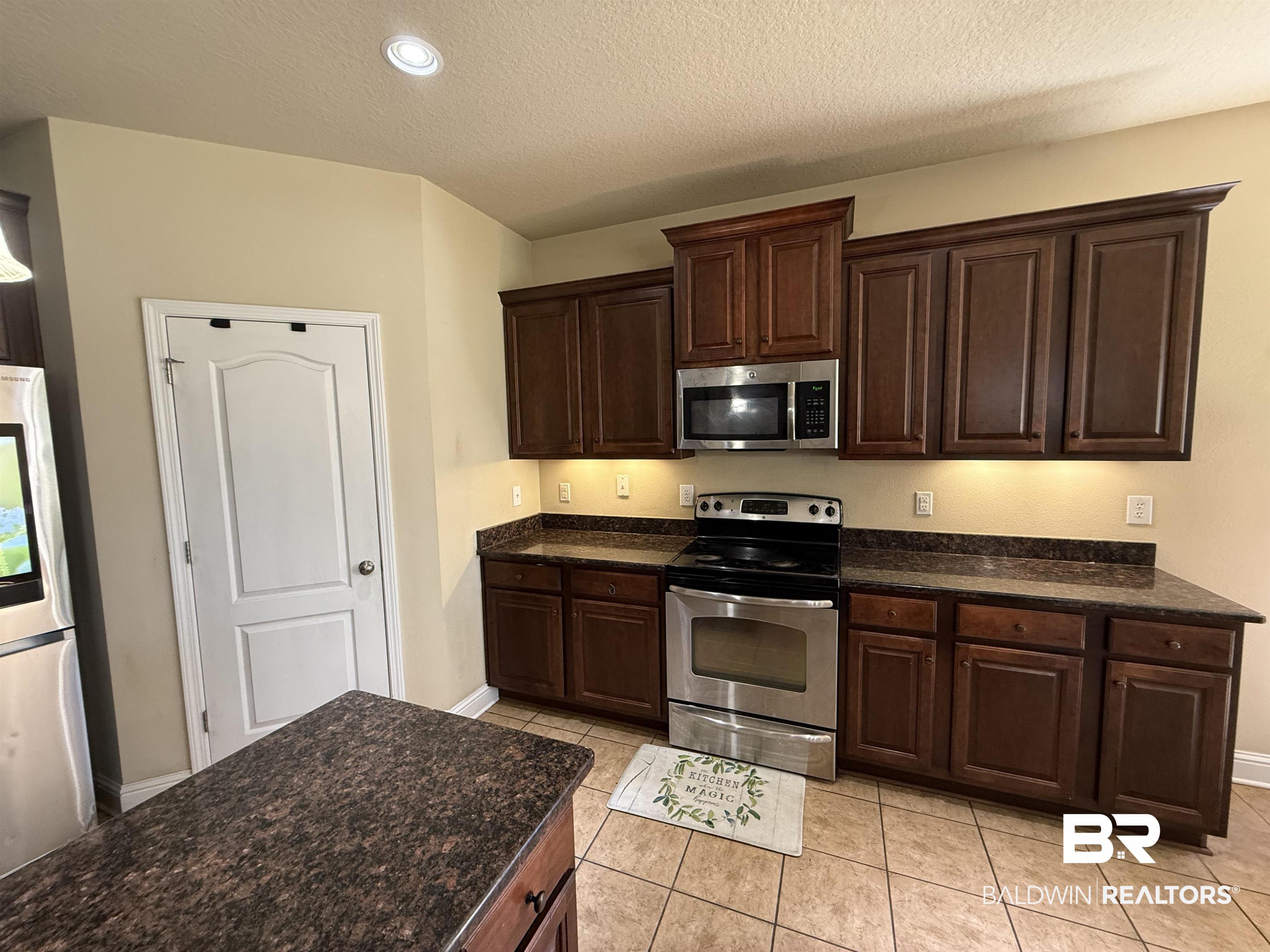 9023 Krystal Ridge Court Daphne, AL 36526 - Photo 16 of 41 Kitchen with dark brown cabinets, appliances with stainless steel finishes, a textured ceiling, light tile patterned floors, and recessed lighting