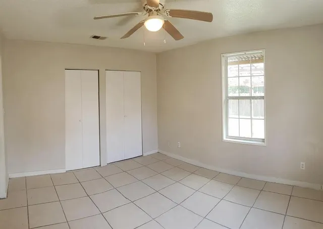 an empty room with chandelier fan and windows