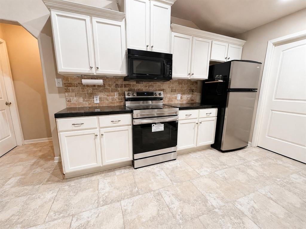 420 Sessums Road Springtown, TX 76082 - Photo 12 of 40 Kitchen featuring white cabinetry, dark countertops, a brick-patterned backsplash, stainless steel appliances, and large format tile flooring