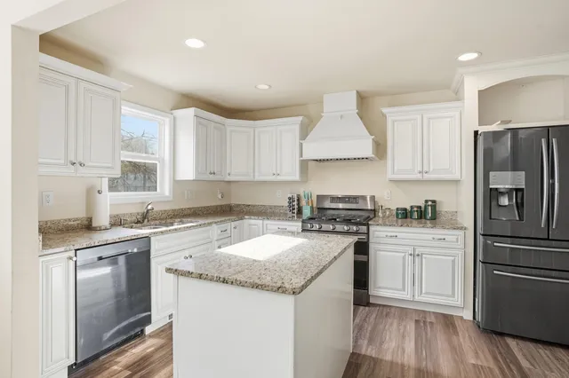 a kitchen with a sink stove a refrigerator and white cabinets with wooden floor
