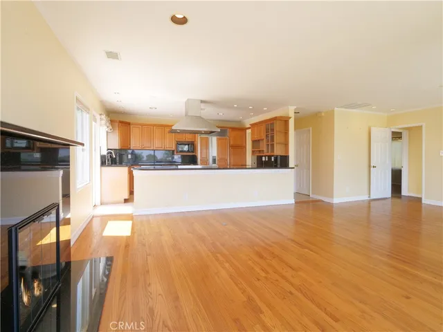 a view of a living room a kitchen with stainless steel appliances granite countertop a stove and a wooden floors