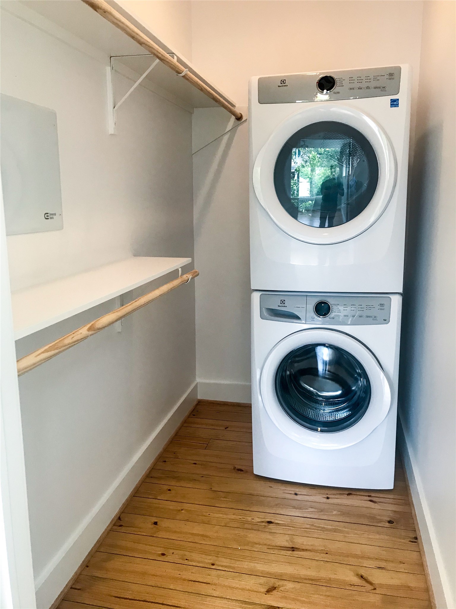 210 Tabor Street Houston, TX 77009 - Photo 16 of 18 This photo shows master closet with a stacked washer and dryer. The space features wooden flooring and a shelf with a hanging rod for additional storage.