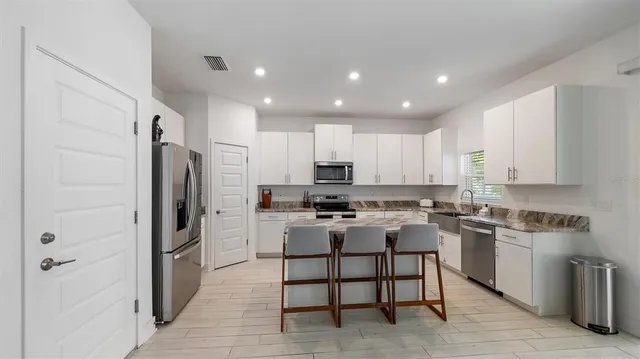 a kitchen with stainless steel appliances granite countertop a stove a sink a refrigerator white cabinets and a refrigerator