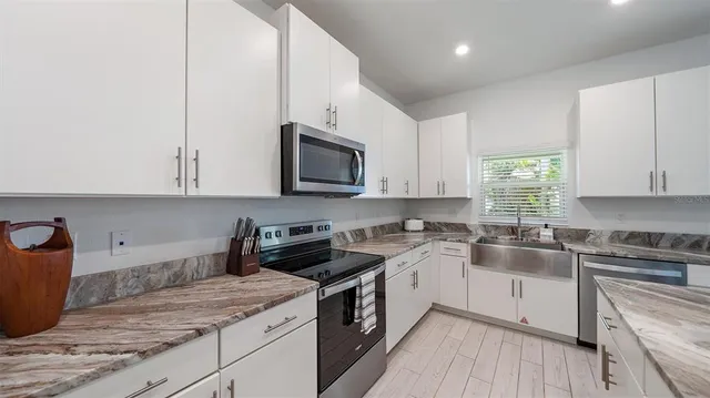 a kitchen with stainless steel appliances granite countertop a stove top oven a refrigerator a sink and chairs