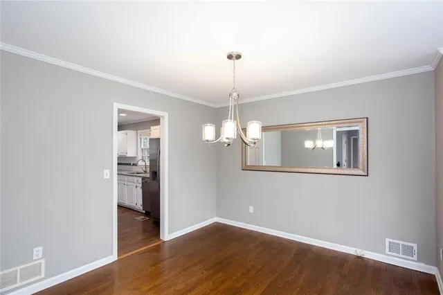 an empty room with wooden floor chandelier and windows