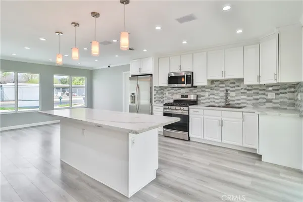 a kitchen with kitchen island granite countertop a stove a sink a refrigerator and white cabinets with wooden floor