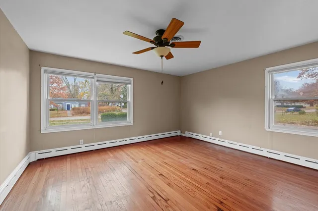 a view of an empty room with wooden floor and a ceiling fan