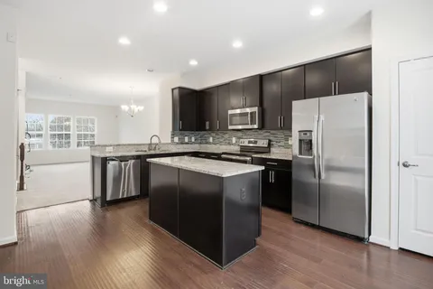 a kitchen with stainless steel appliances granite countertop a refrigerator a sink a stove a microwave and island with wooden floor