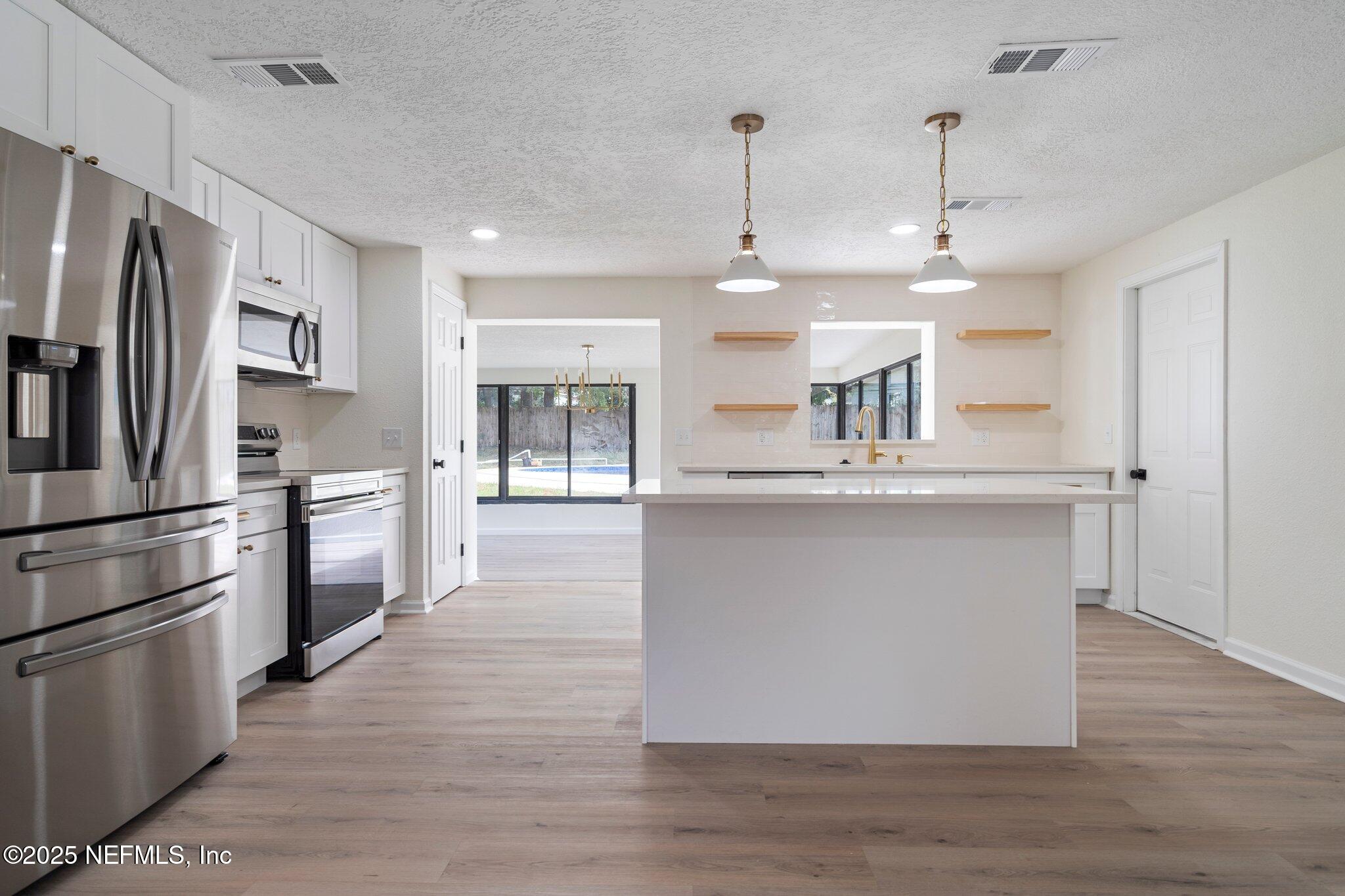 560 Aquarius Concourse Orange Park, FL 32073 - Photo 9 of 32 a kitchen with stainless steel appliances kitchen island granite countertop a refrigerator a stove a sink and white cabinets with wooden floors