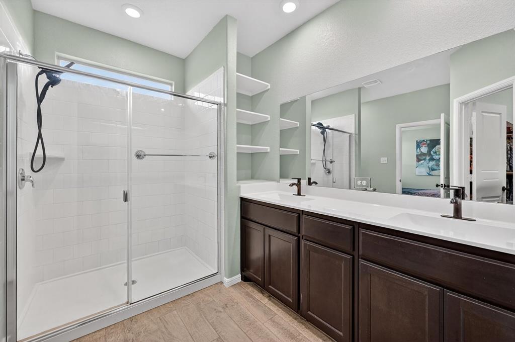 9604 Cherryville Road Fort Worth, TX 76108 - Photo 20 of 40 Spacious bathroom featuring a glass-enclosed shower with white subway tile, a dual vanity with dark wood-finish cabinetry, a large wall-mounted mirror, and wood-finish flooring