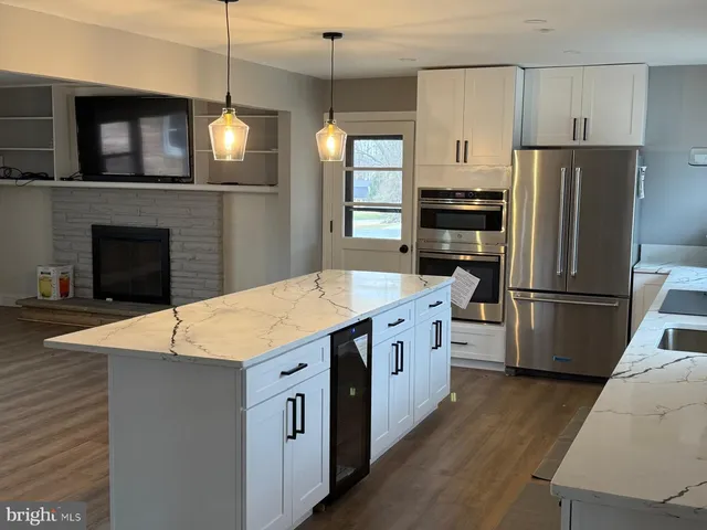 a kitchen with stainless steel appliances kitchen island granite countertop a refrigerator a stove a sink dishwasher and a fireplace with wooden floor