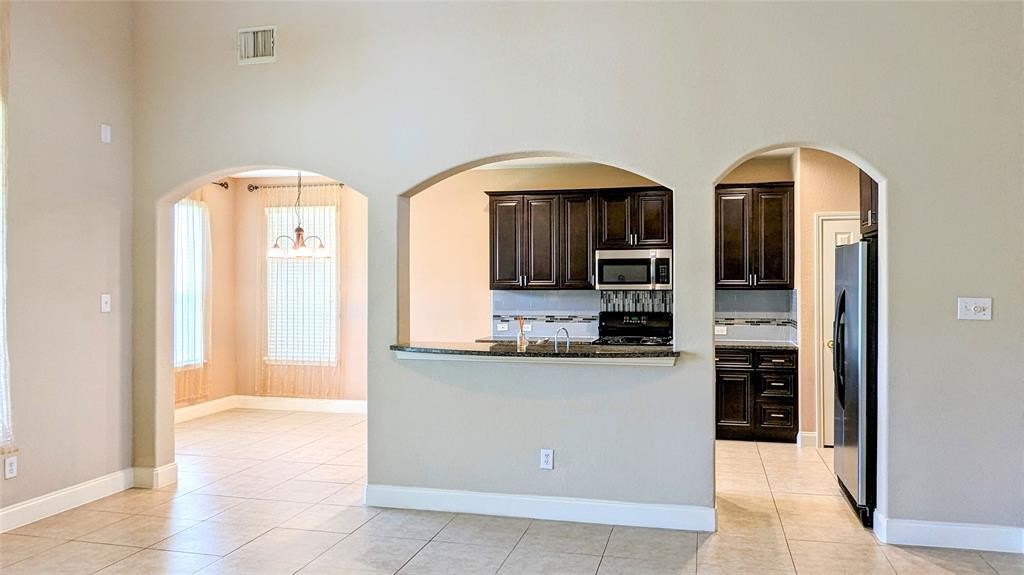 20909 Springport Court Katy, TX 77450 - Photo 14 of 39 Elegant kitchen with dark cabinetry and granite countertops, complemented by an open archway design and adjacent cozy dining area.