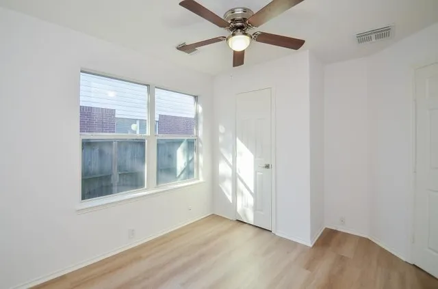 an empty room with wooden floor fan and windows