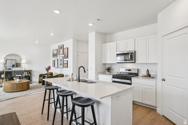 2097 North Ostler Peak Road, Unit 115 Heber City, UT 84032 - Photo 30 of 33 Open-concept kitchen featuring a spacious island with sink and seating, white cabinetry, stainless steel appliances, and light-toned wood-finish flooring throughout