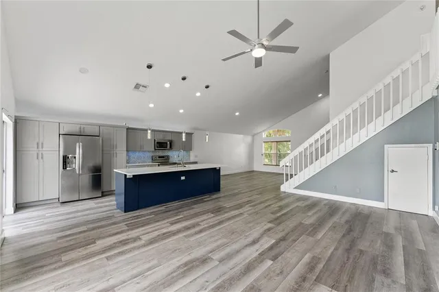 a living room with stainless steel appliances kitchen island wooden floors and ceiling fan