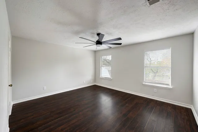 an empty room with wooden floor ceiling fan and windows