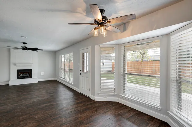 a view of an empty room with wooden floor fireplace and a window