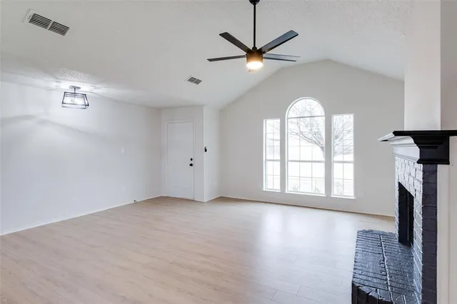 an empty room with wooden floor fan and windows