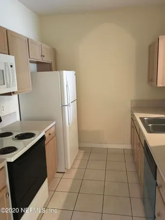 a view of an empty room with wooden floor and a kitchen