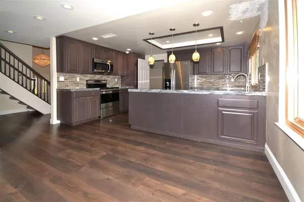 a living room with stainless steel appliances kitchen island granite countertop a refrigerator a stove top oven and a sink with wooden floor
