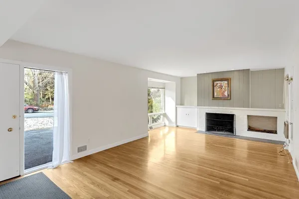 a view of an empty room with wooden floor fireplace and a window