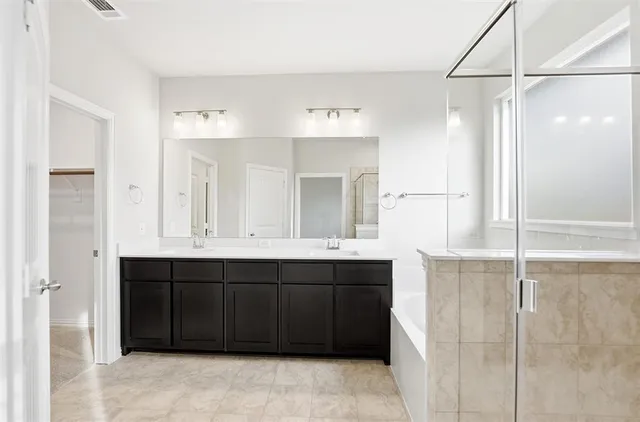 a bathroom with a double vanity sink a large mirror and a bathtub