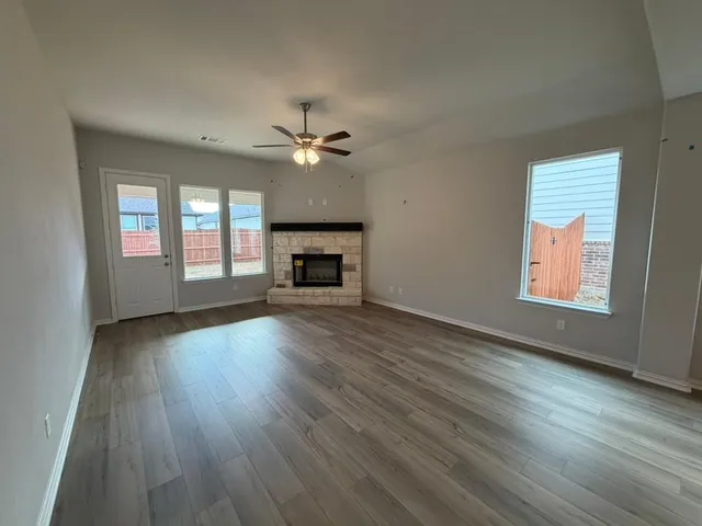 an empty room with wooden floor fireplace and windows
