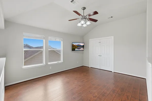 an empty room with wooden floor chandelier fan and windows