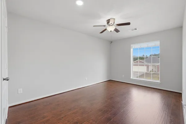 an empty room with wooden floor fan and windows