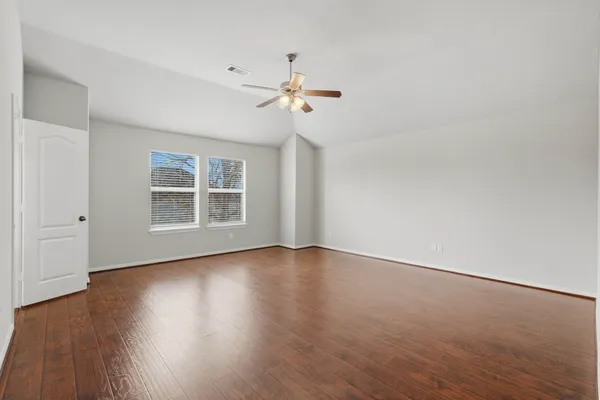 an empty room with wooden floor ceiling fan and windows