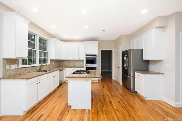 a kitchen with stainless steel appliances a stove top oven a sink a refrigerator white cabinets and wooden floor