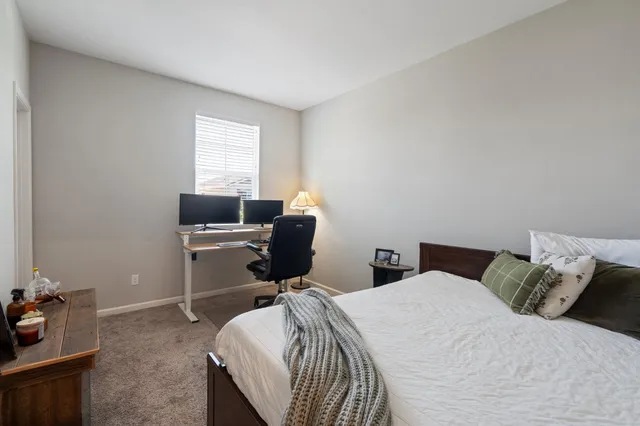 a bedroom with a bed computer on desk and a window