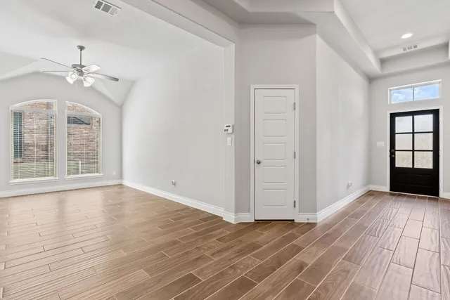 an empty room with wooden floor chandelier fan and windows