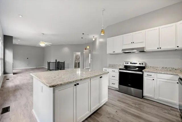 a kitchen with stainless steel appliances granite countertop a sink dishwasher a stove and white cabinets with wooden floor