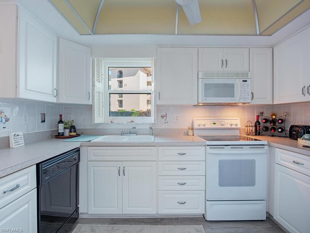 53 High Point Circle West, Unit 101 Naples, FL 34103 - Photo 5 of 18 a kitchen with white cabinets and white appliances