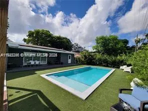 a view of a swimming pool with lawn chairs plants and large trees