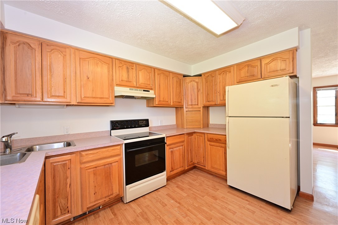 8280 Lafayette Road Lodi, OH 44254 - Photo 17 of 35 Kitchen featuring a textured ceiling, white refrigerator, brown cabinets, light countertops, light hardwood flooring, and electric range oven