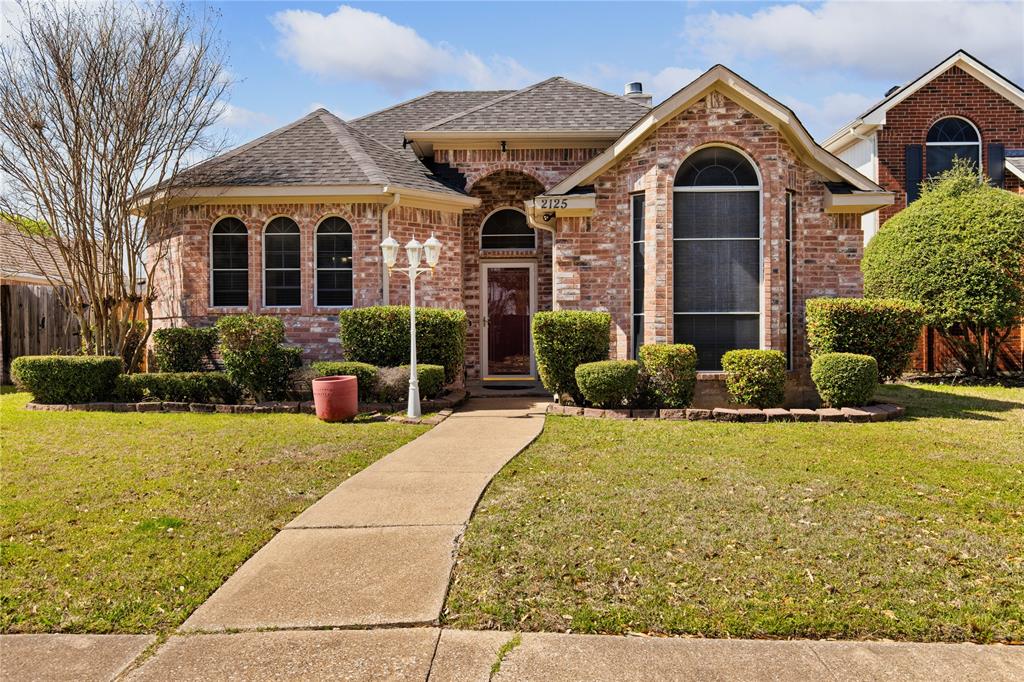 View of front of home featuring brick siding, a front yard, a shingled roof, and fence