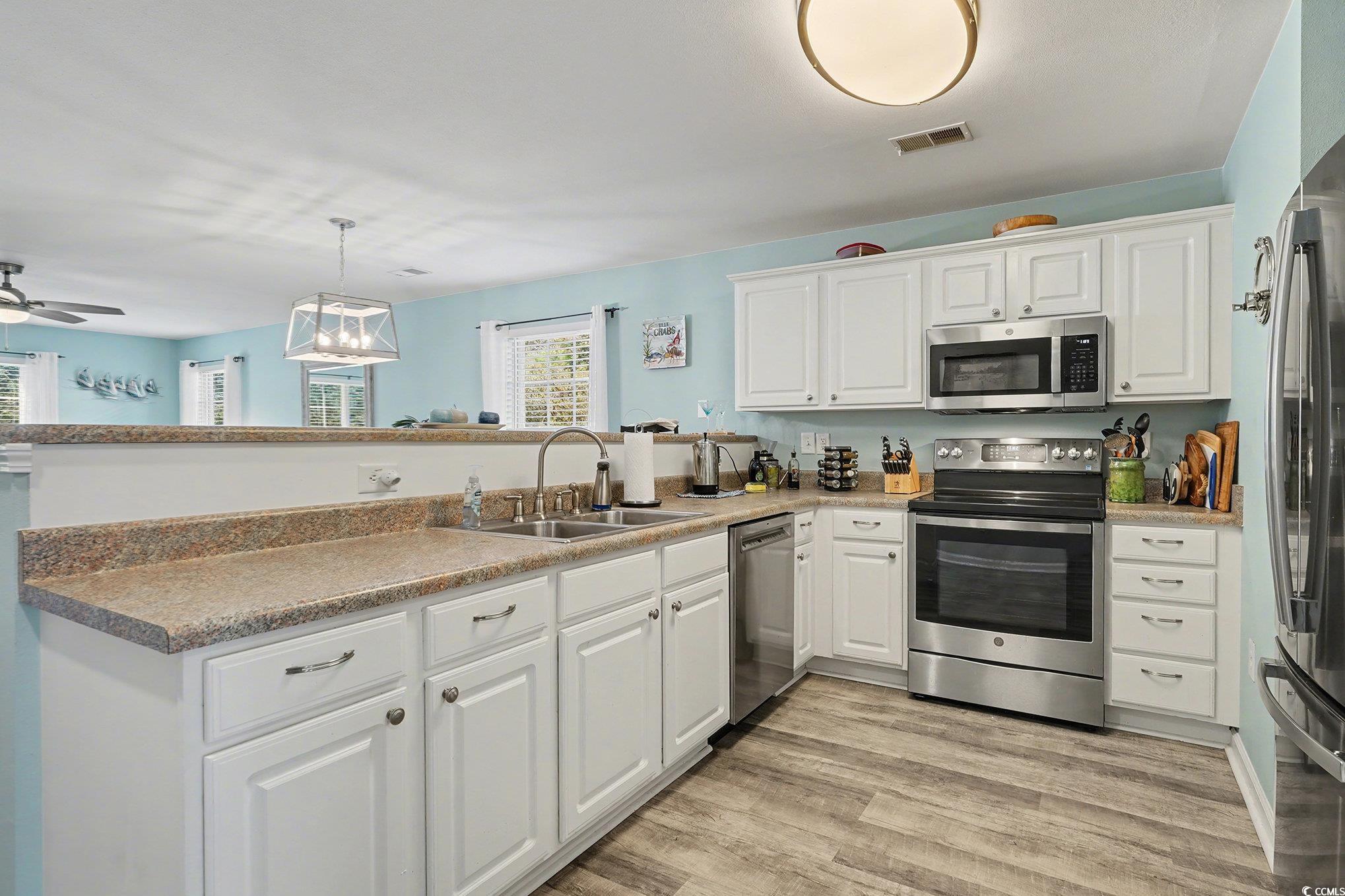 725 Blue Stem Drive, Unit 66B Pawleys Island, SC 29585 - Photo 11 of 30 Kitchen featuring appliances with stainless steel finishes, white cabinets, hanging light fixtures, light wood-type flooring, and a peninsula