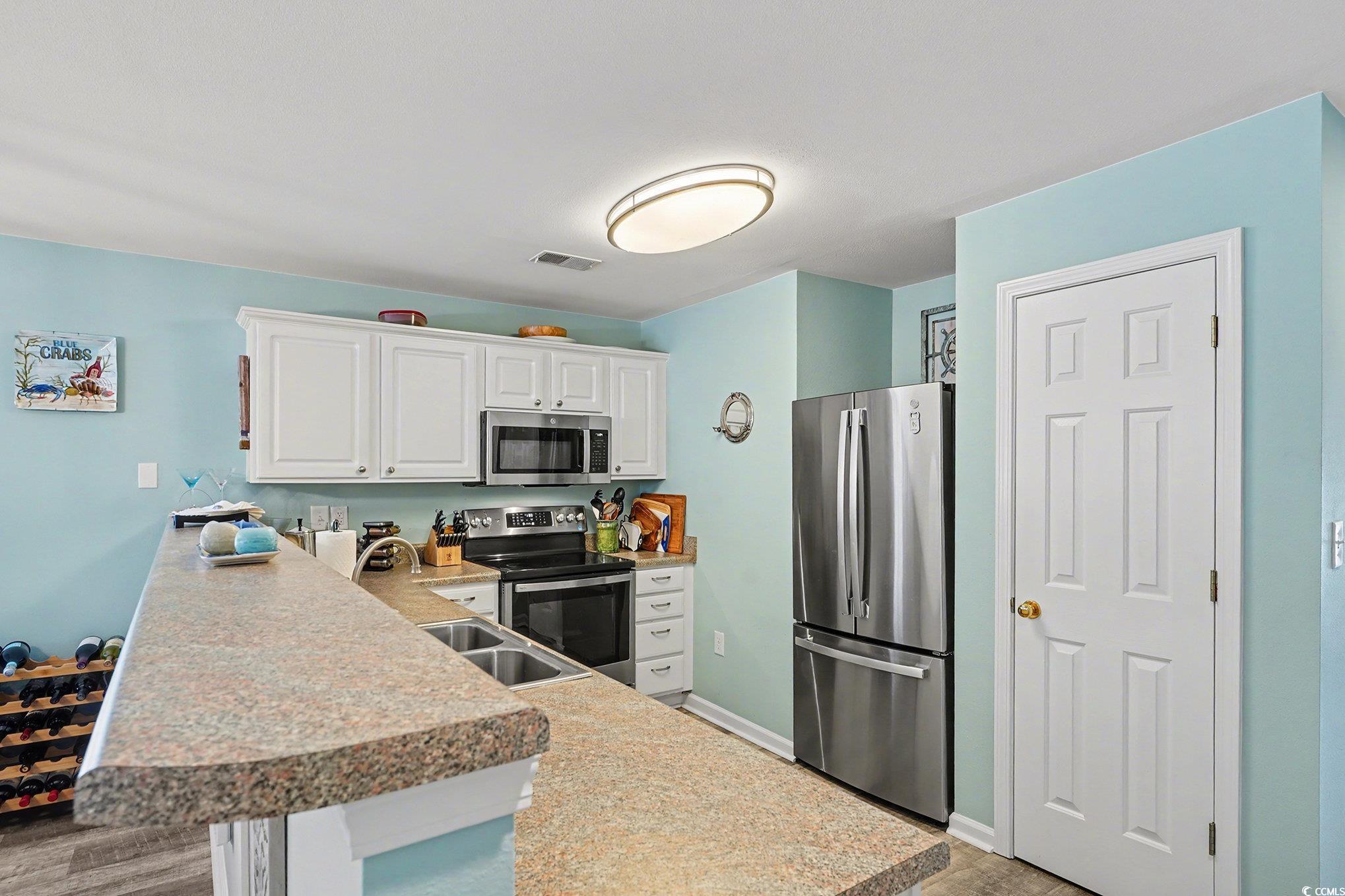 725 Blue Stem Drive, Unit 66B Pawleys Island, SC 29585 - Photo 12 of 30 Kitchen featuring appliances with stainless steel finishes, white cabinets, a peninsula, light countertops, and light wood finished floors