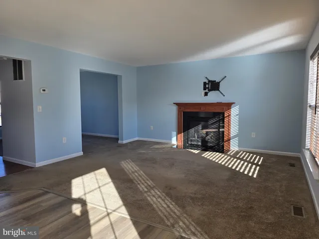 a view of an empty room with wooden floor fireplace and a window