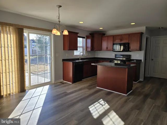 a kitchen with stainless steel appliances granite countertop a stove top oven a sink dishwasher a refrigerator and a dining table with wooden floor