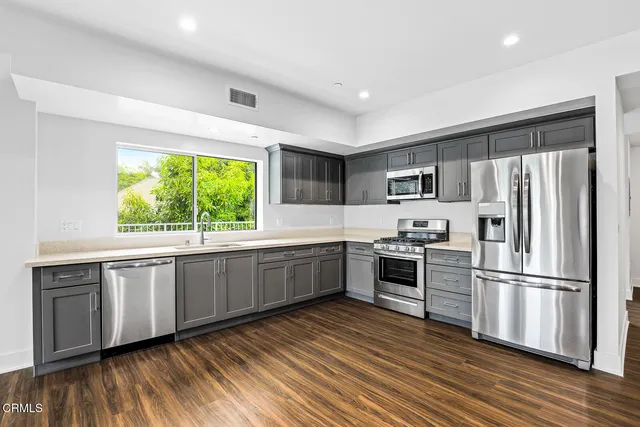 a kitchen with stainless steel appliances granite countertop a refrigerator a stove top oven a sink and dishwasher with wooden floor