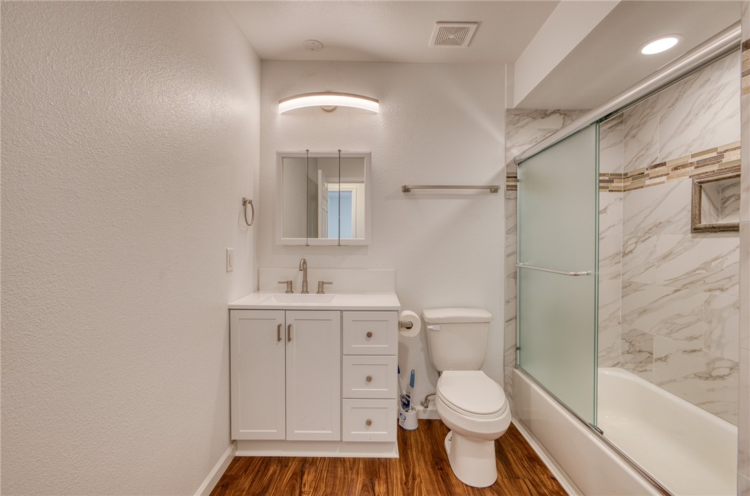 2053 Regents Road Mohave Valley, AZ 86440 - Photo 21 of 65 The bathroom features hardwood flooring, a vanity with a white countertop and white cabinetry, and a shower-tub combination with a sliding frosted glass door and marble-style tiling